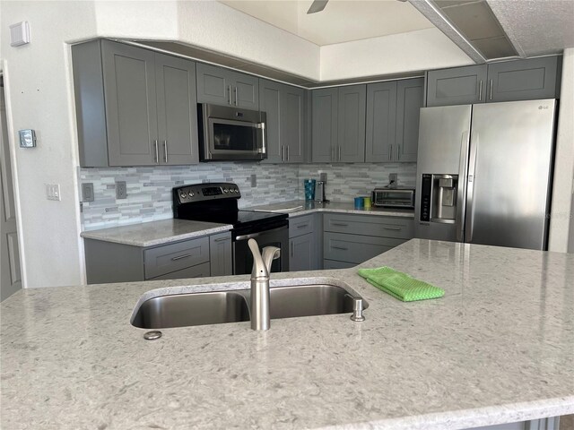 kitchen with decorative backsplash, a sink, stainless steel appliances, light stone countertops, and gray cabinets