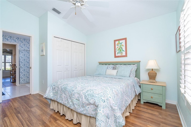 bedroom featuring wood finished floors, visible vents, baseboards, vaulted ceiling, and a closet