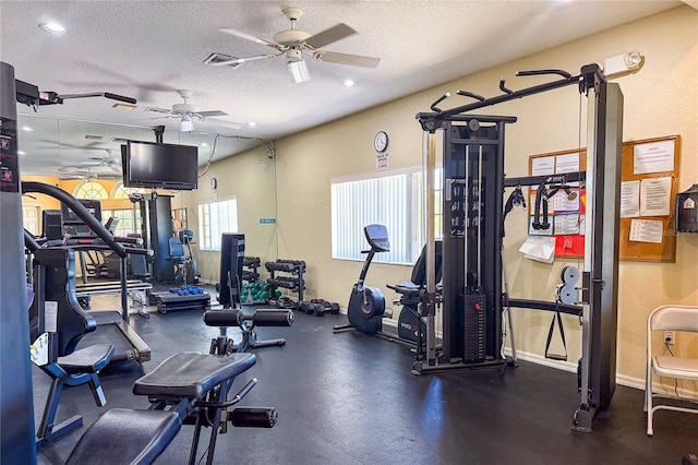 gym with a textured ceiling, visible vents, a ceiling fan, and baseboards