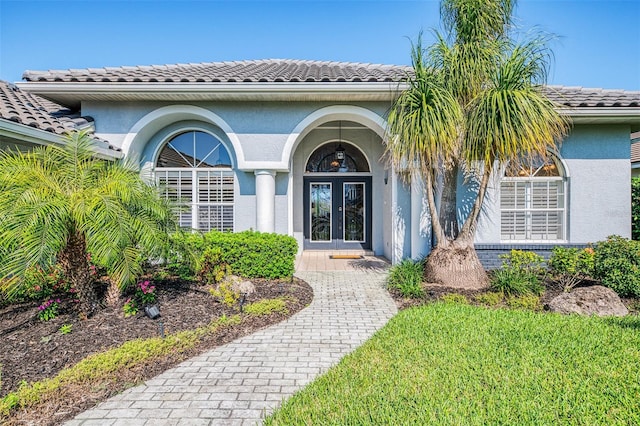 entrance to property featuring stucco siding, a tiled roof, and french doors