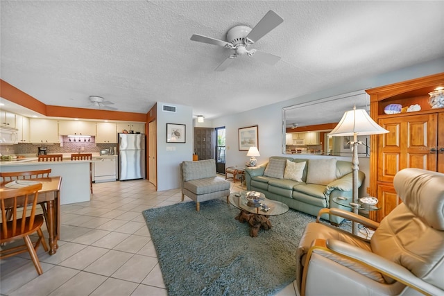 living area with light tile patterned floors, a ceiling fan, visible vents, and a textured ceiling