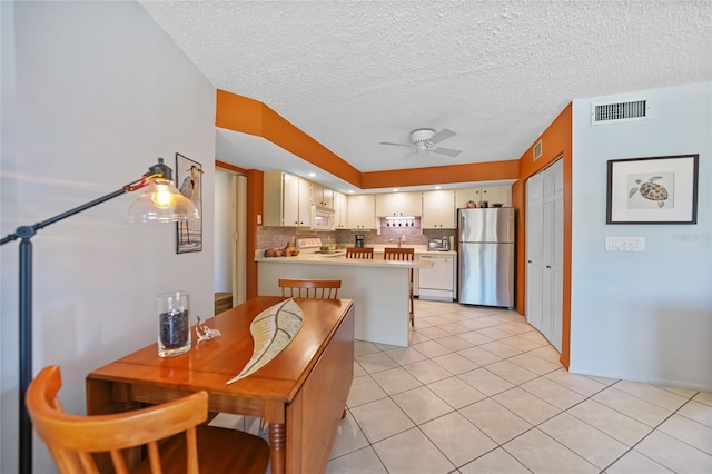 kitchen with tasteful backsplash, visible vents, a peninsula, white appliances, and a ceiling fan