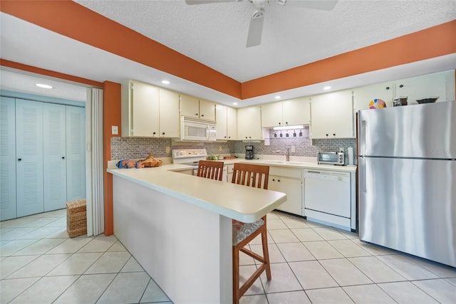 kitchen with a sink, white appliances, a peninsula, light countertops, and light tile patterned floors