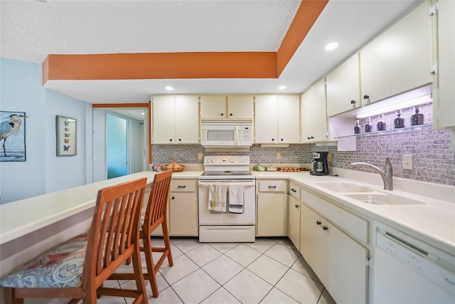 kitchen with tasteful backsplash, light countertops, cream cabinets, white appliances, and a sink