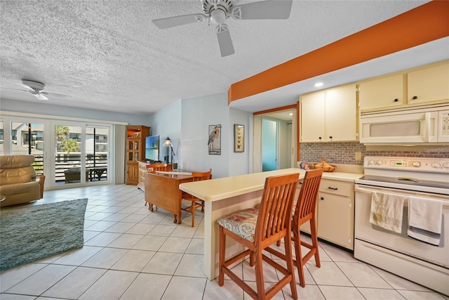 kitchen with cream cabinets, a textured ceiling, open floor plan, white appliances, and light tile patterned floors