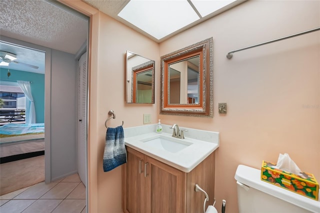 ensuite bathroom with tile patterned floors, toilet, a textured ceiling, ceiling fan, and vanity