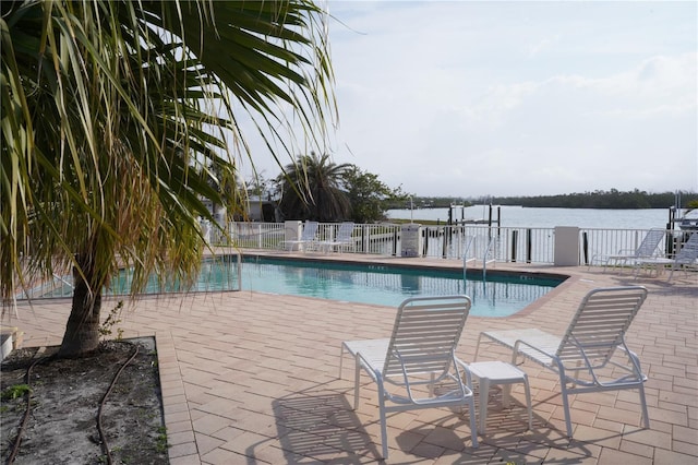 pool featuring a patio area, a water view, and fence