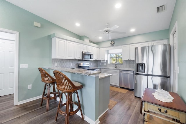 kitchen with light stone counters, stainless steel appliances, a peninsula, and white cabinetry