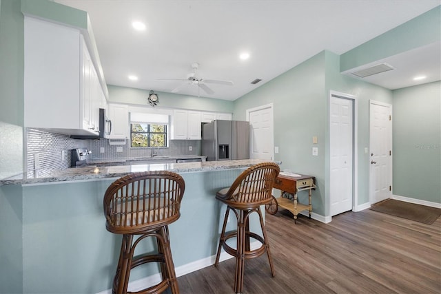 kitchen with a kitchen bar, white cabinetry, stainless steel appliances, a peninsula, and light stone countertops