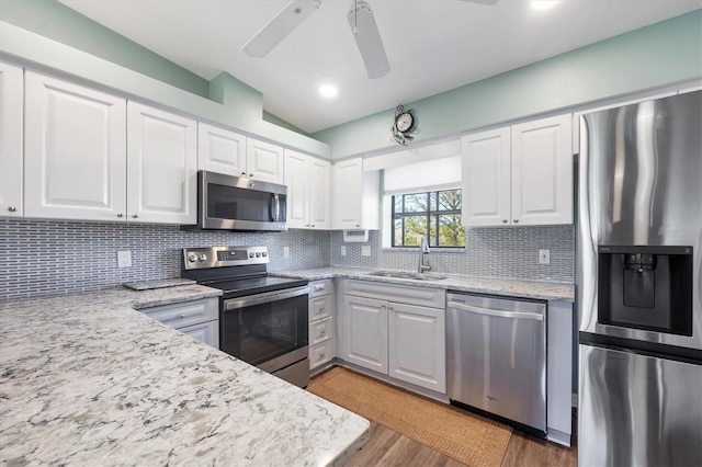 kitchen with a sink, white cabinetry, stainless steel appliances, light wood finished floors, and decorative backsplash