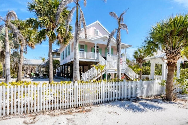 raised beach house featuring covered porch, a fenced front yard, and stairway