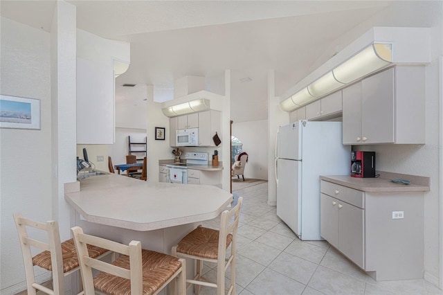 kitchen with white appliances, light tile patterned floors, a peninsula, light countertops, and a kitchen bar