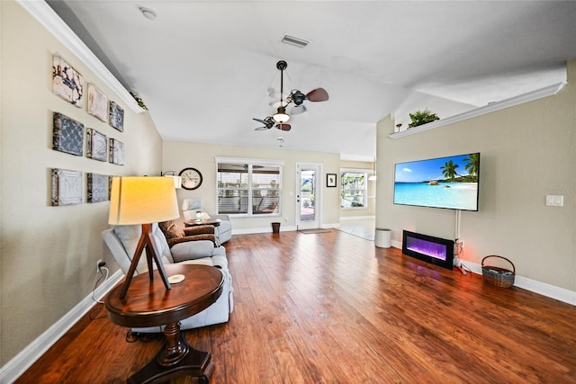 living area with wood finished floors, visible vents, baseboards, vaulted ceiling, and a glass covered fireplace