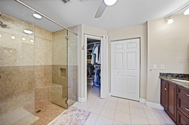 bathroom with a textured ceiling, a shower stall, tile patterned flooring, ceiling fan, and vanity