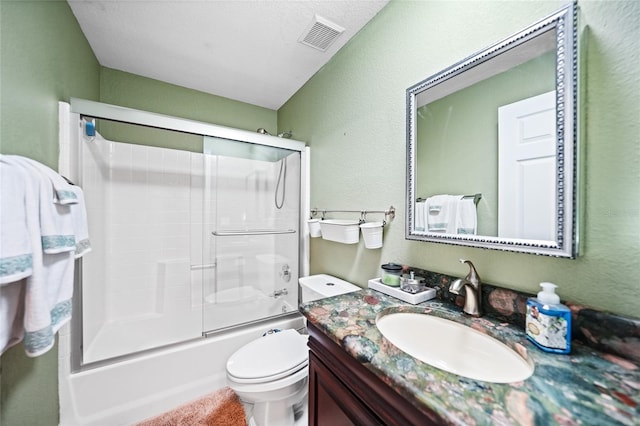 full bath with vanity, visible vents, bath / shower combo with glass door, toilet, and a textured wall