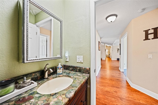 bathroom with vanity, wood finished floors, baseboards, and a textured wall