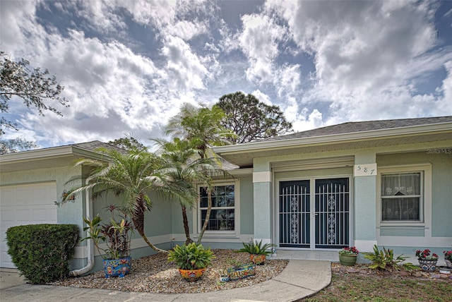 doorway to property with stucco siding, a shingled roof, and a garage