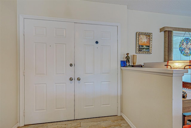 entryway featuring light wood-style floors, a textured ceiling, and baseboards