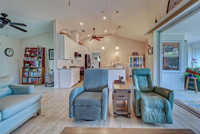 living room with vaulted ceiling, a ceiling fan, and light wood-style floors