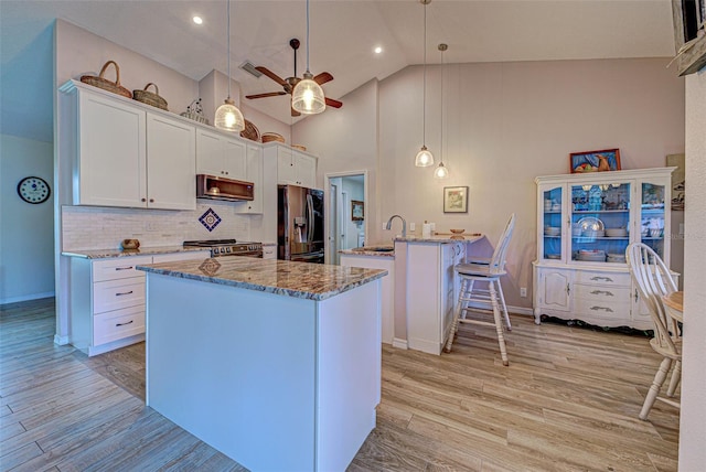 kitchen with light wood finished floors, light stone countertops, stainless steel appliances, a kitchen bar, and white cabinetry