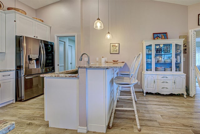 kitchen featuring light wood-style flooring, white cabinetry, light stone countertops, stainless steel fridge, and a kitchen bar