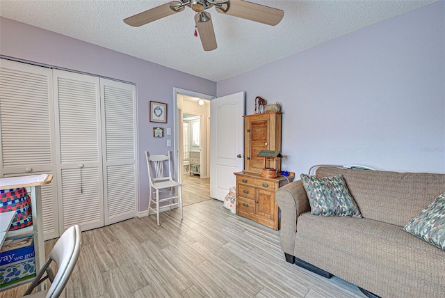 living area featuring a textured ceiling, ceiling fan, baseboards, and light wood-style floors