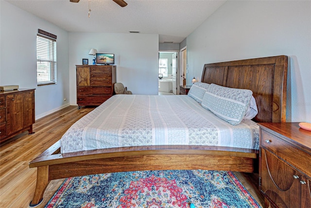 bedroom featuring ensuite bathroom, wood finished floors, a ceiling fan, visible vents, and baseboards