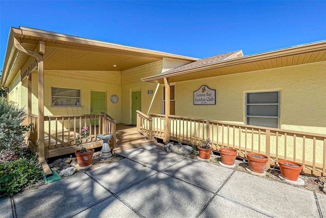 entrance to property featuring covered porch, a shingled roof, and stucco siding