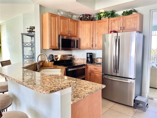 kitchen featuring a sink, light stone counters, stainless steel appliances, a peninsula, and light tile patterned flooring