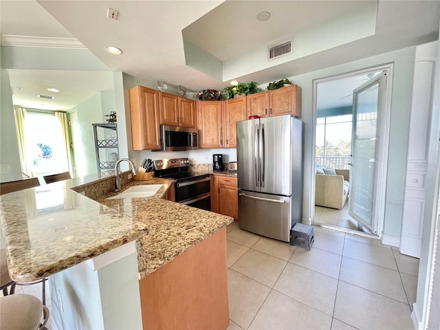 kitchen featuring light stone counters, visible vents, a peninsula, a sink, and appliances with stainless steel finishes