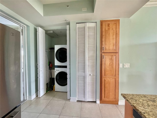 laundry room featuring stacked washer / drying machine, baseboards, light tile patterned flooring, and laundry area