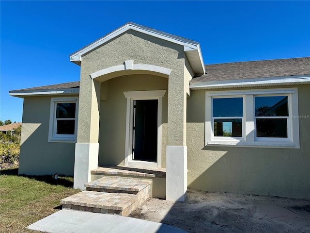 entrance to property with roof with shingles and stucco siding