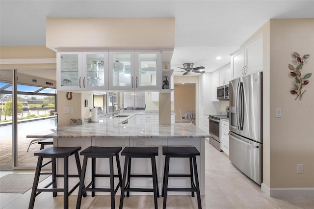 kitchen featuring glass insert cabinets, appliances with stainless steel finishes, a peninsula, white cabinets, and a sink