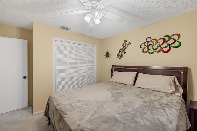 carpeted bedroom featuring a closet, visible vents, a textured ceiling, and a ceiling fan