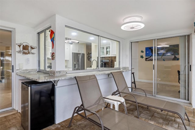 kitchen with light stone counters, a breakfast bar, stainless steel fridge with ice dispenser, freestanding refrigerator, and white cabinets