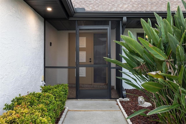 view of exterior entry featuring stucco siding and a shingled roof