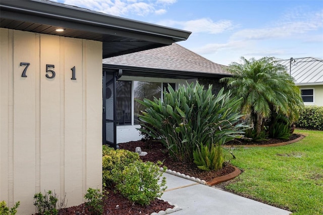 view of exterior entry featuring a lawn and a shingled roof