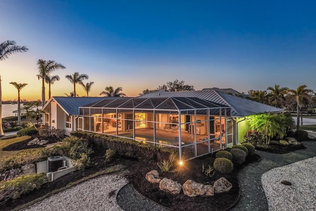 back of house at dusk with glass enclosure and metal roof