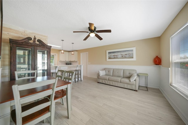 living room with a textured ceiling, light wood-style floors, a wainscoted wall, and ceiling fan