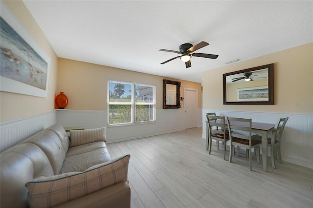 living room with light wood finished floors, visible vents, wainscoting, and ceiling fan