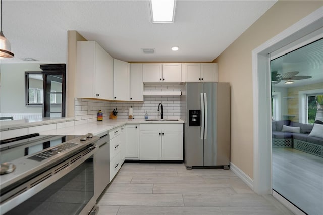 kitchen featuring light countertops, decorative backsplash, appliances with stainless steel finishes, white cabinets, and a sink