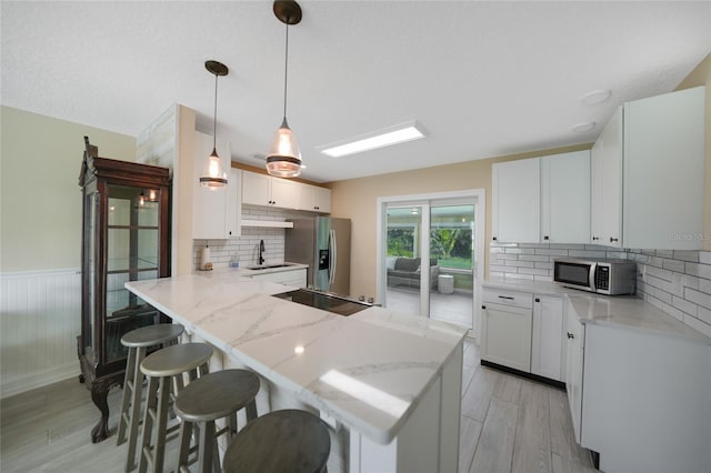 kitchen with a sink, appliances with stainless steel finishes, a breakfast bar area, a peninsula, and wainscoting