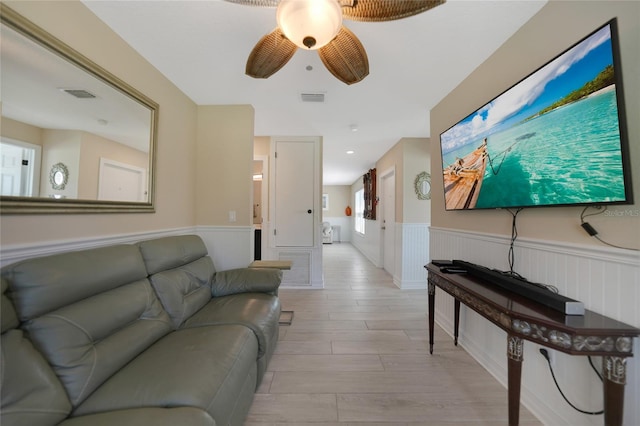 living area with visible vents, wainscoting, light wood-style flooring, and a ceiling fan