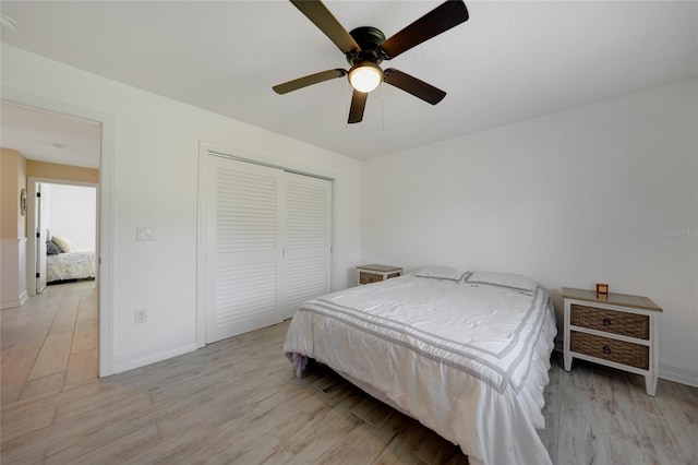 bedroom with light wood finished floors, ceiling fan, baseboards, and a closet