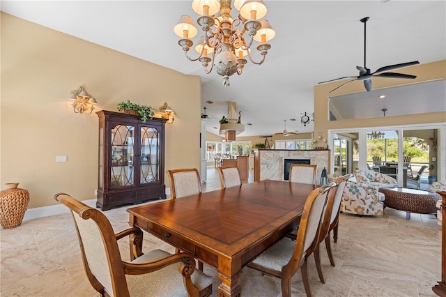 dining room with baseboards, vaulted ceiling, a fireplace, and ceiling fan with notable chandelier