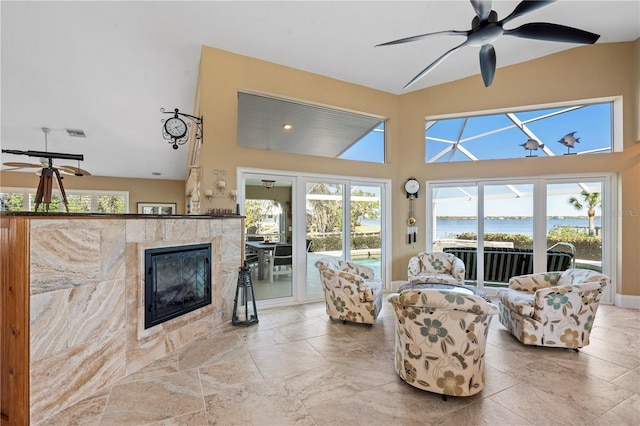 living area with a water view, a towering ceiling, a ceiling fan, and a tile fireplace