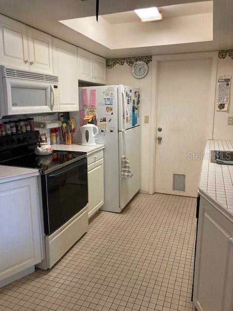 kitchen with white cabinets, white appliances, a tray ceiling, and light countertops