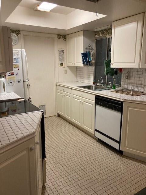 kitchen with tile counters, tasteful backsplash, white cabinetry, a sink, and white appliances