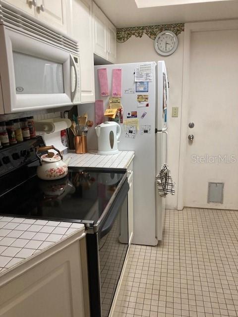 kitchen with white appliances, white cabinetry, tile countertops, and light tile patterned flooring