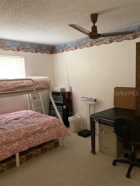 carpeted bedroom featuring ceiling fan and a textured ceiling